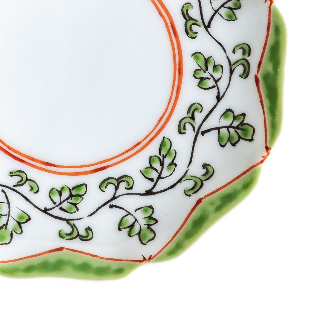 A white ceramic plate with a scalloped edge, featuring a delicate vine pattern in green and red around the border.