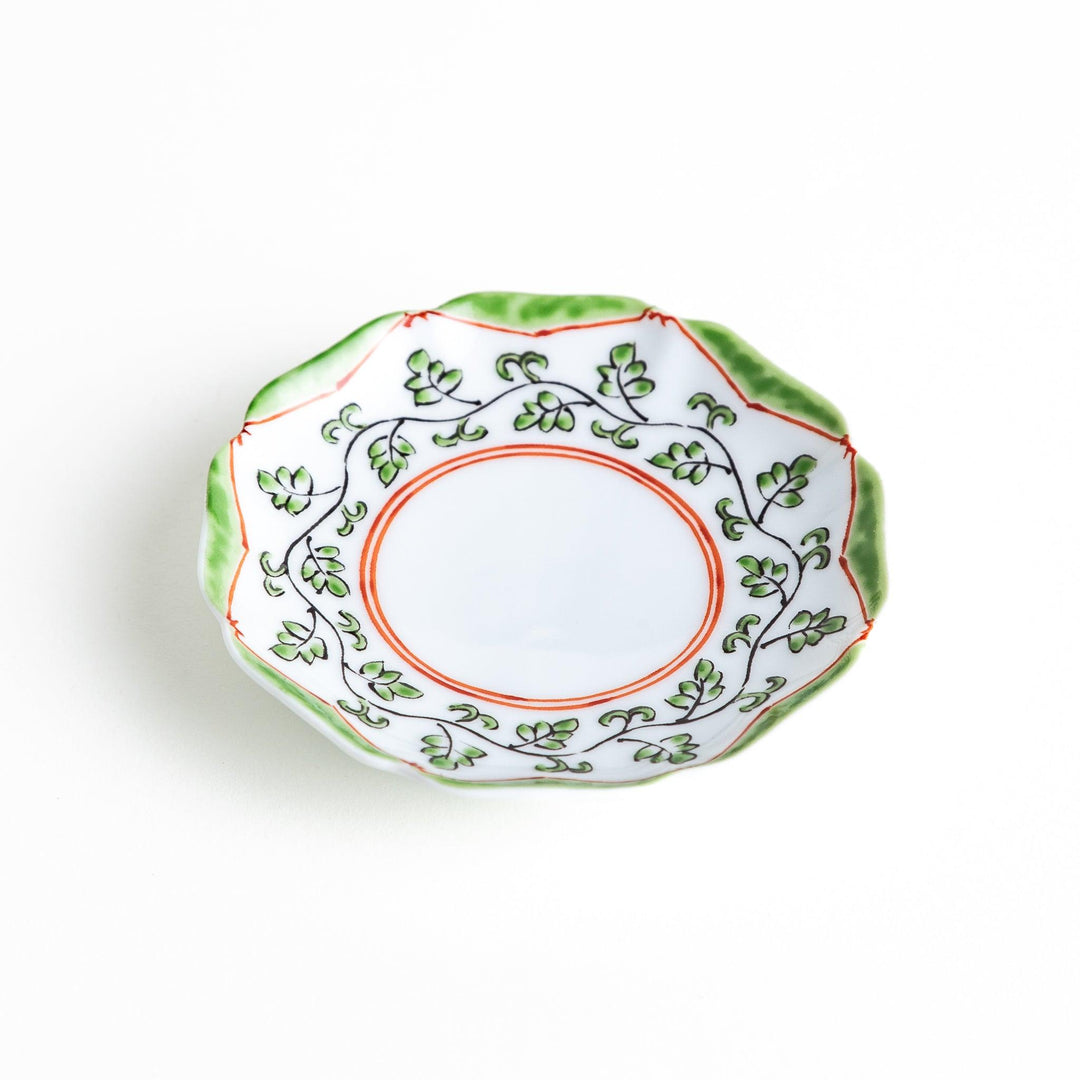 A white ceramic plate with a scalloped edge, featuring a delicate vine pattern in green and red around the border.