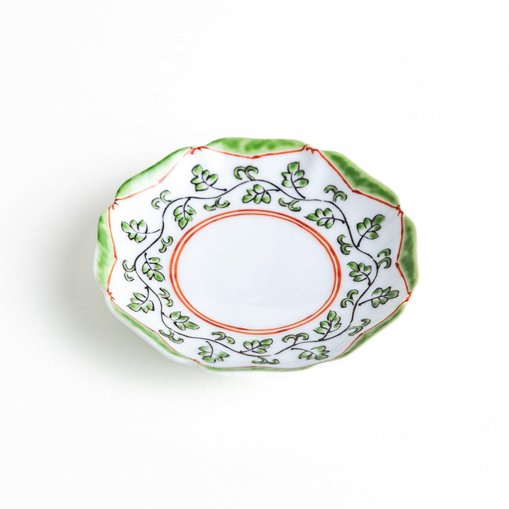 A white ceramic plate with a scalloped edge, featuring a delicate vine pattern in green and red around the border.