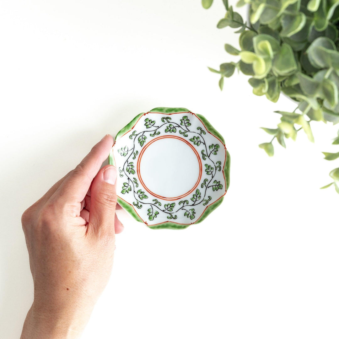 A white ceramic plate with a scalloped edge, featuring a delicate vine pattern in green and red around the border.