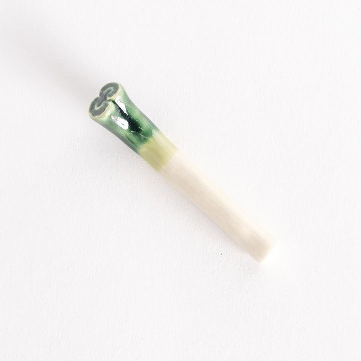 A ceramic long green onion chopsticks rest in glossy green and white hues, shaped to mimic a fresh green onion stalk.