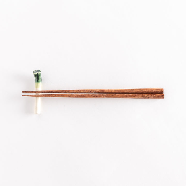 Full view of the long green onion chopsticks rest with chopsticks placed across its body.