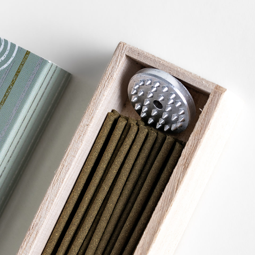 Incense in a light wooden box with earthy green sticks, featuring an elegant soft green package adorned with white circular patterns for a serene aesthetic.