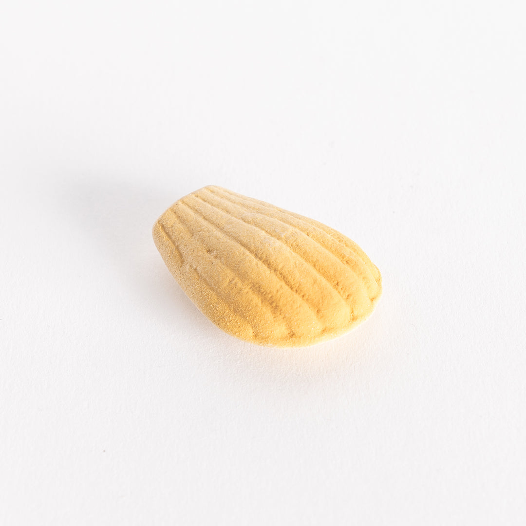 A slightly angled view of the ceramic golden madeleine chopstick rest, displaying its detailed ridges and rounded edges.