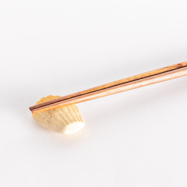 A close-up view of a ceramic golden madeleine chopstick rest holding a pair of chopsticks, highlighting its intricate ridged details.