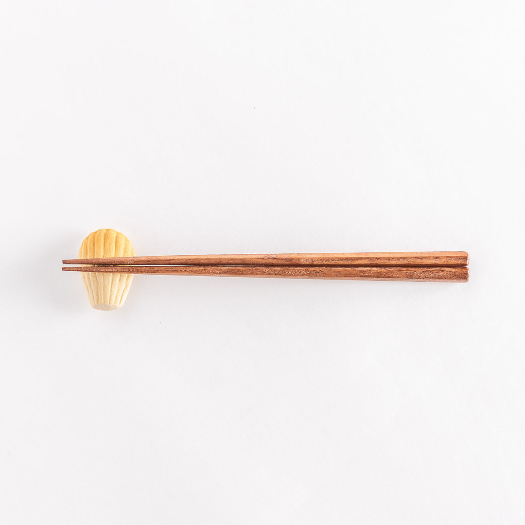 A wide view of the ceramic golden madeleine chopstick rest with chopsticks placed on it, emphasizing its elegant design and soft tones.