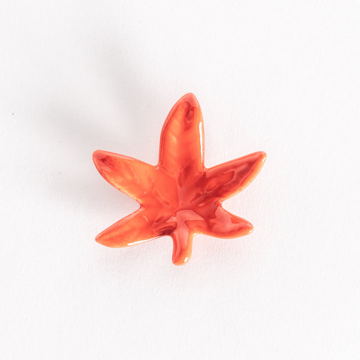 Bright red maple leaf-shaped chopsticks rest displayed against a white background.