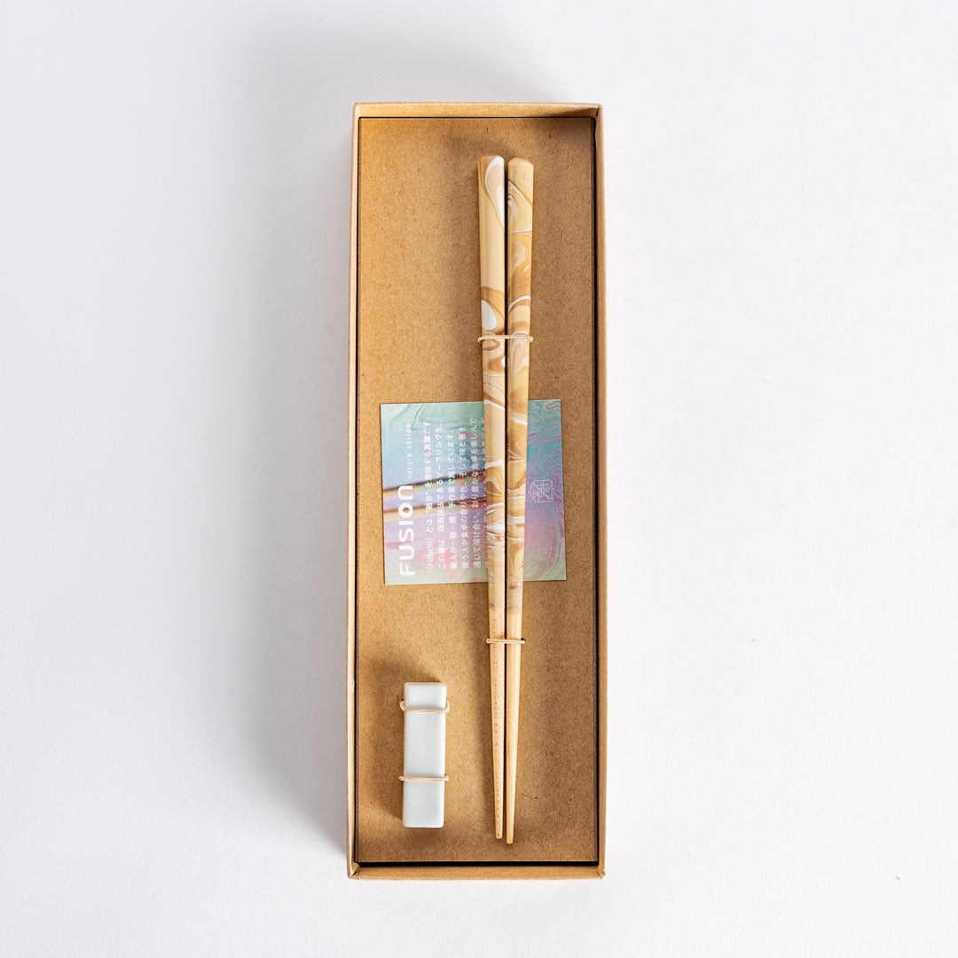 Top view of caramel-patterned chopsticks in a brown Fusion gift box, alongside a porcelain holder and decorative insert.