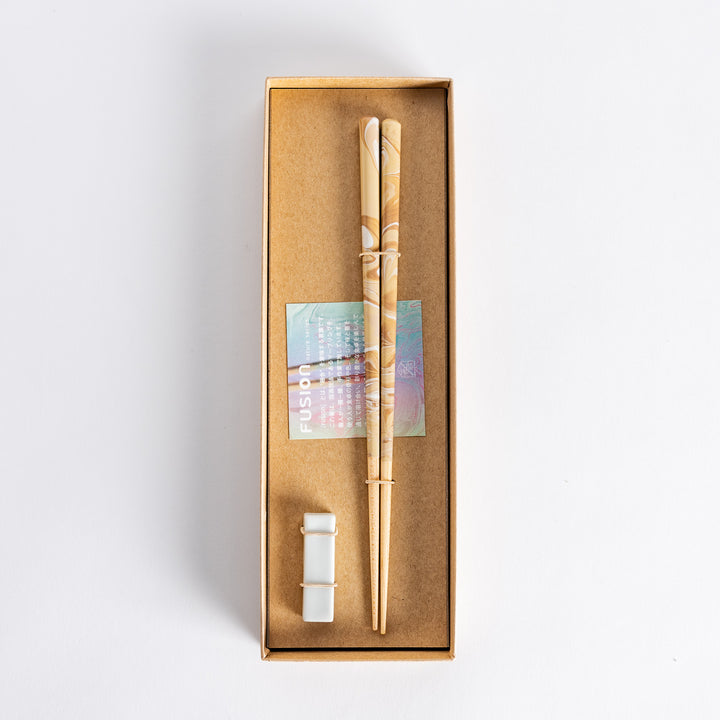 Top view of caramel-patterned chopsticks in a brown Fusion gift box, alongside a porcelain holder and decorative insert.