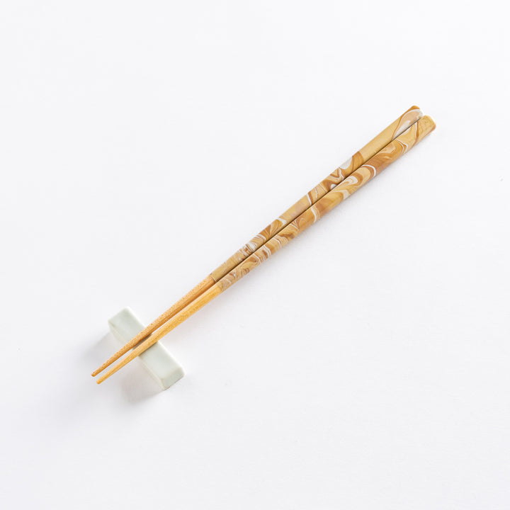 Caramel-patterned chopsticks resting on a minimalist white porcelain holder, angled on a white background.