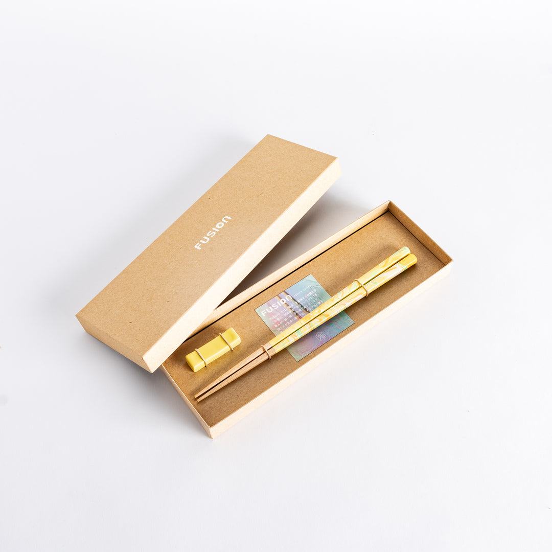 This chopsticks set comes in a minimalistic kraft box with vibrant yellow, orange, and green marbled tips, paired with a matching rest for a fresh look.