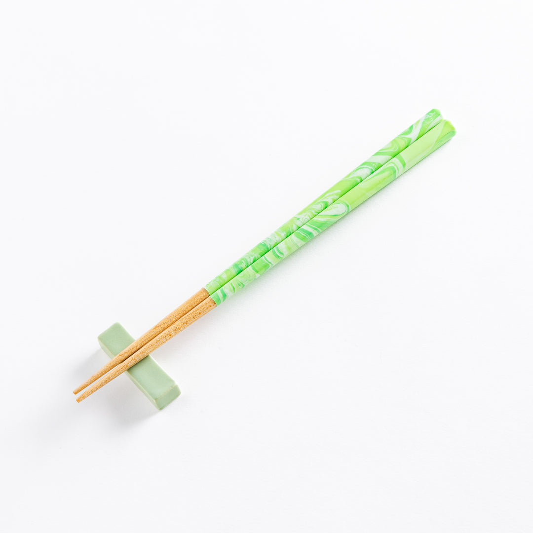 Mint green marbled chopsticks with wooden tips resting on a matching chopstick rest, offering a stylish and functional design.