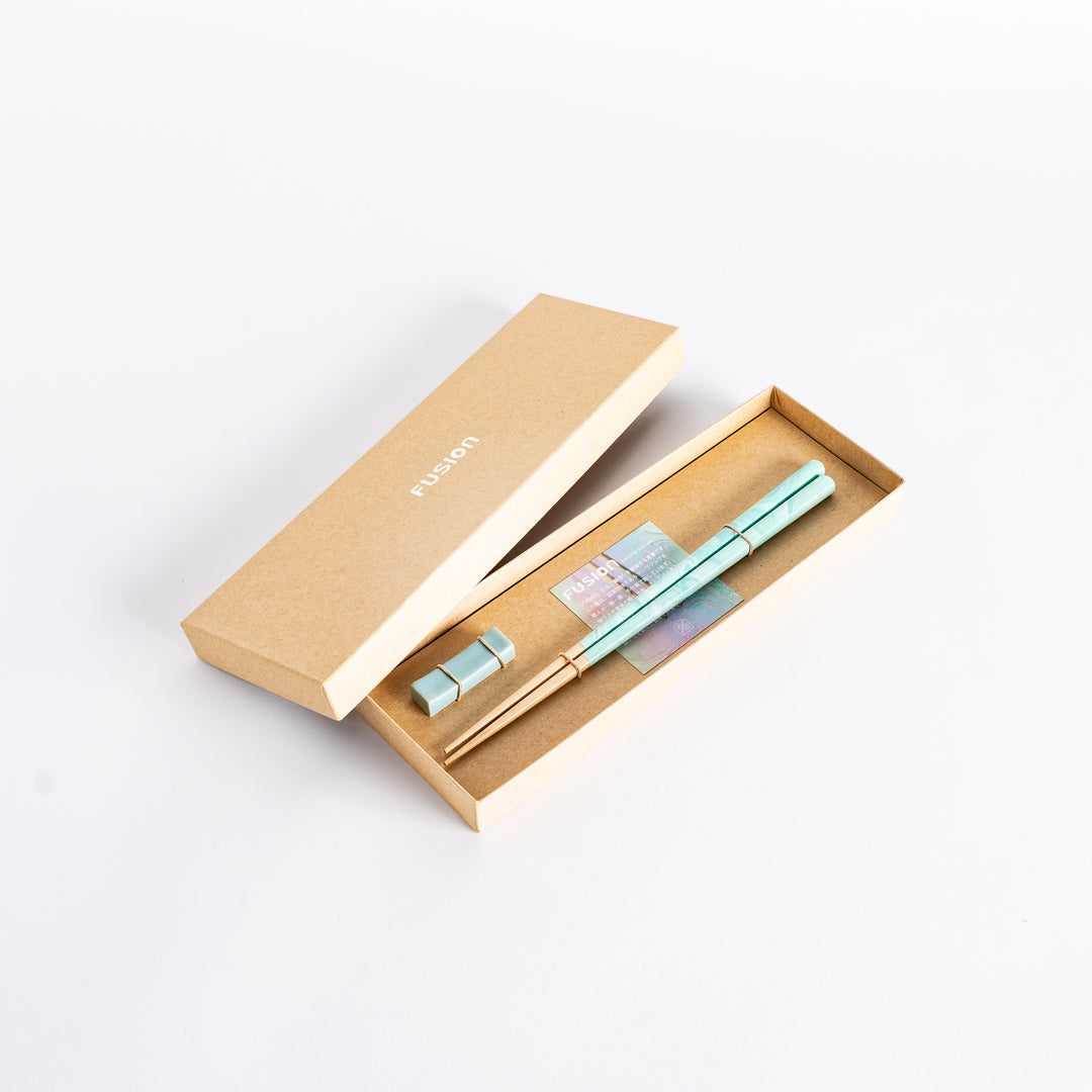 Top view of aqua chopsticks with a marbled finish, secured with a simple band, resting in a stylish packaging.