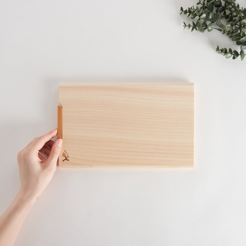 Hand holding a small hinoki cutting board, showing its natural wood grain and compact design.