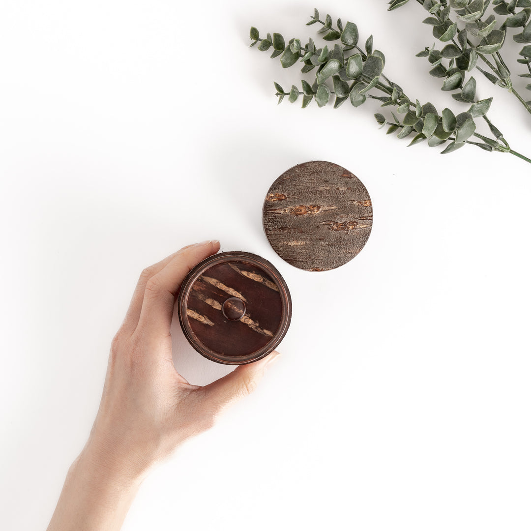 Hand holding a rustic cherry bark tea canister with a separate lid, showcasing the natural beauty of the bark, perfect for storing and preserving tea.