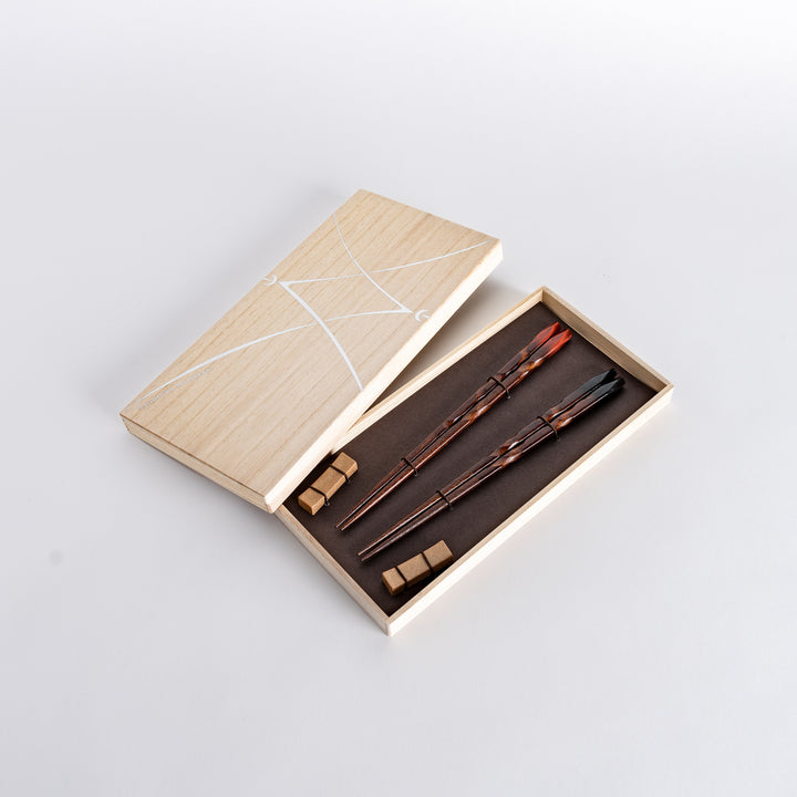 Hand holding dark brown chopsticks with a unique, textured carved design, showing their size and style.