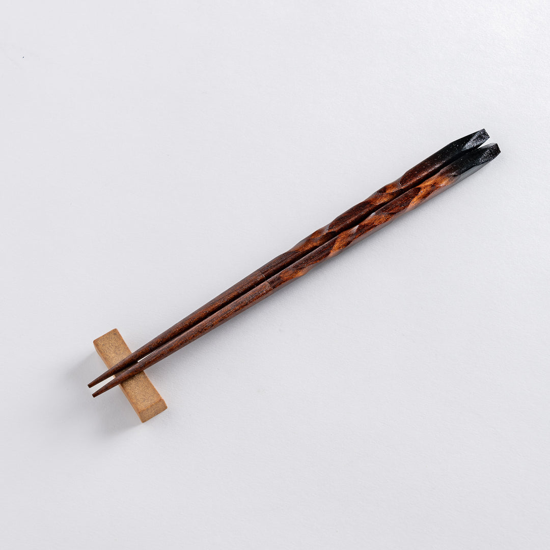 A detailed view of the chopsticks resting on a square beige holder, emphasizing the smooth, polished finish of the wood.