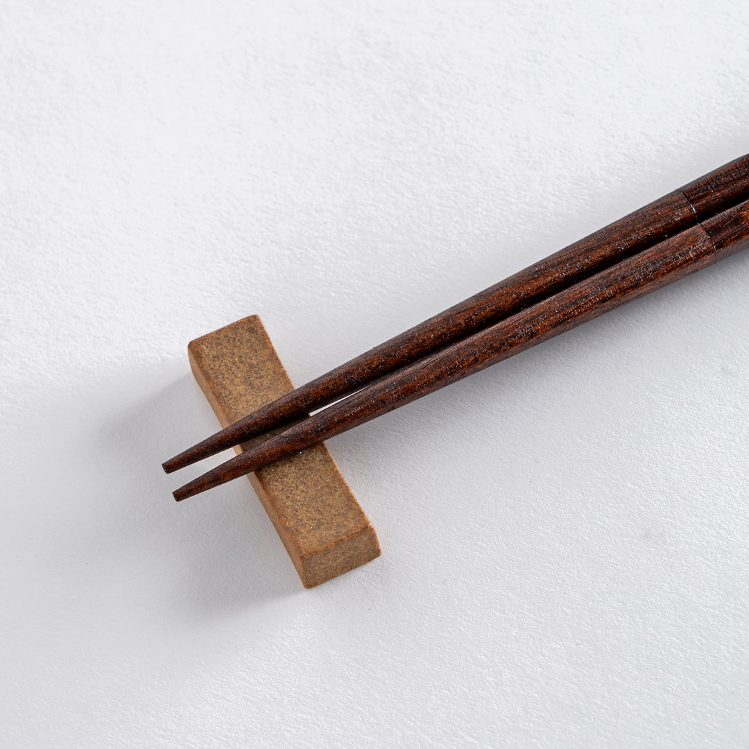 Carved chopsticks with a beautiful dark red gradient, resting on a simple beige block rest, adding elegance to your table.