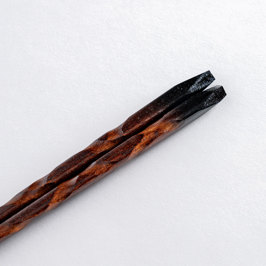 A close-up of chopsticks with a gradient finish, transitioning from dark wood to a vibrant crimson red at the tips, showcasing a unique design.