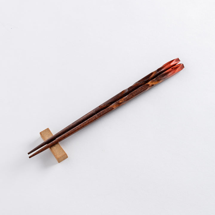 A dark wooden chopsticks with finely tapered tips resting on a simple rectangular chopstick rest, showcasing a smooth, elegant finish.