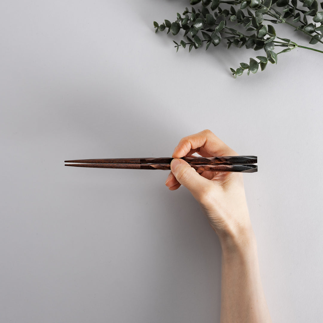 A pair of intricately carved chopsticks, with dark brown wood gradually transitioning to red and black tips, showcasing the elegant craftsmanship.