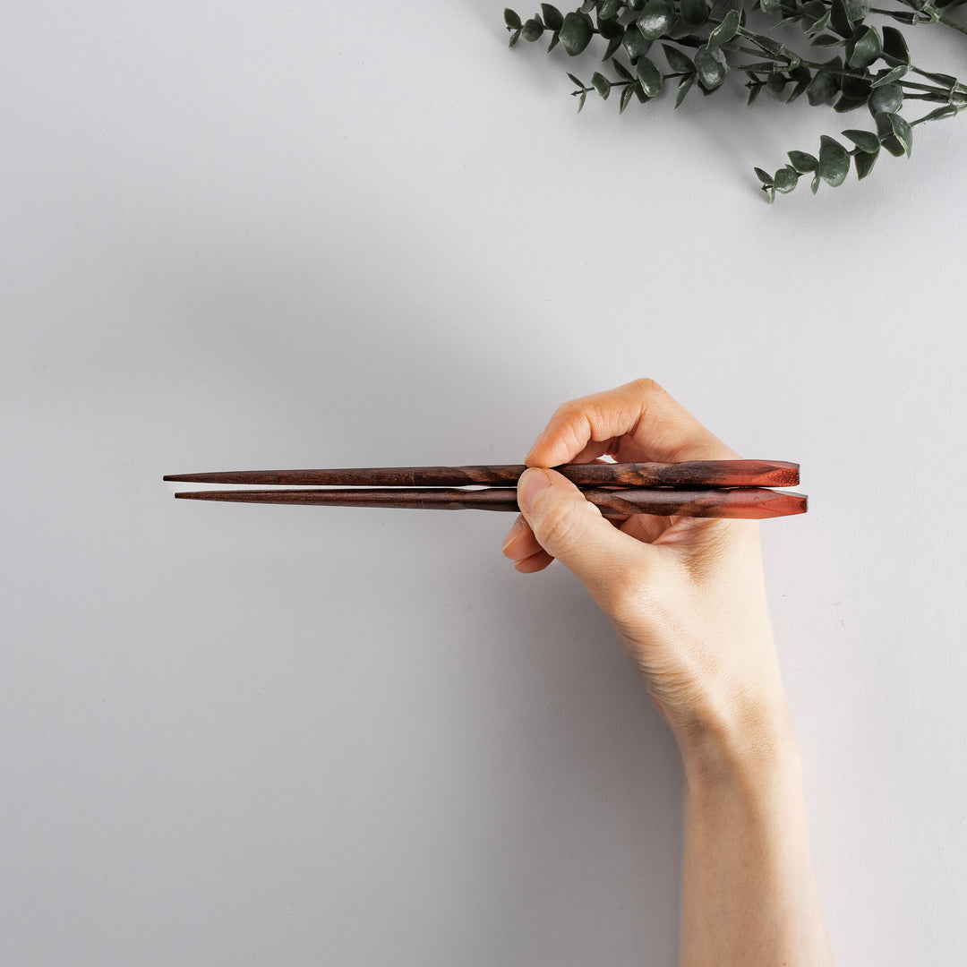 Hand holding red-brown chopsticks with a carved texture, demonstrating a comfortable grip and elegant design.