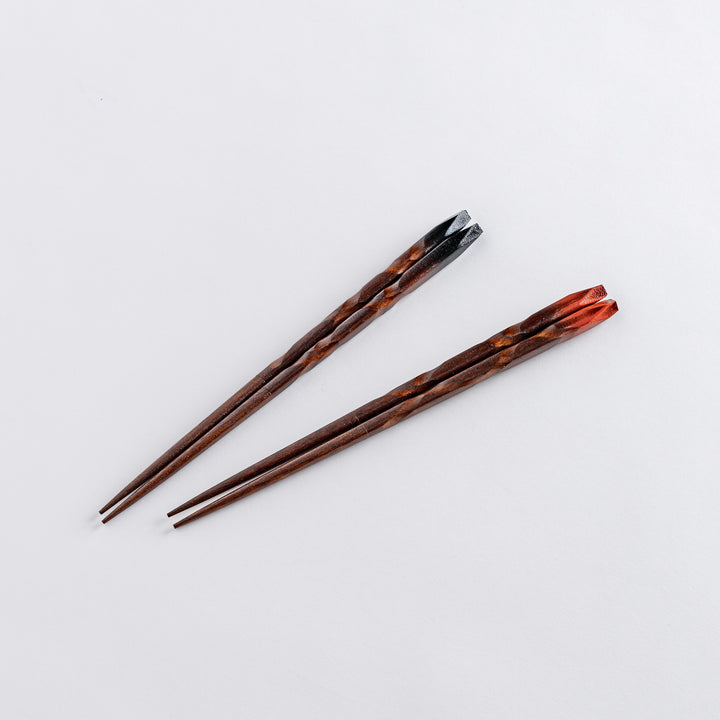 Chopsticks with blackened tips, delicately crafted with a spiral pattern and a beige chopstick rest placed underneath.