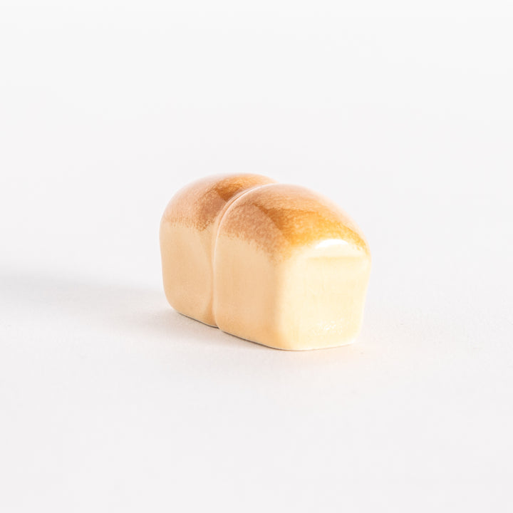 A ceramic chopsticks rest shaped like a loaf of milk bread with a glossy golden-brown top.