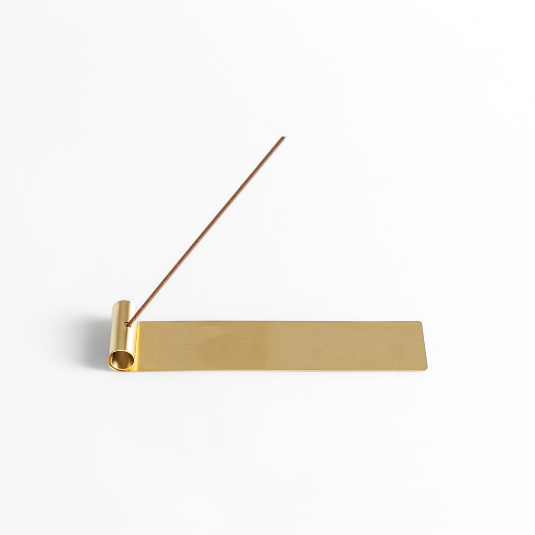 Minimalist brass incense holder with a sleek rolled-edge design, securely holding a single incense stick while the flat base catches falling ash.