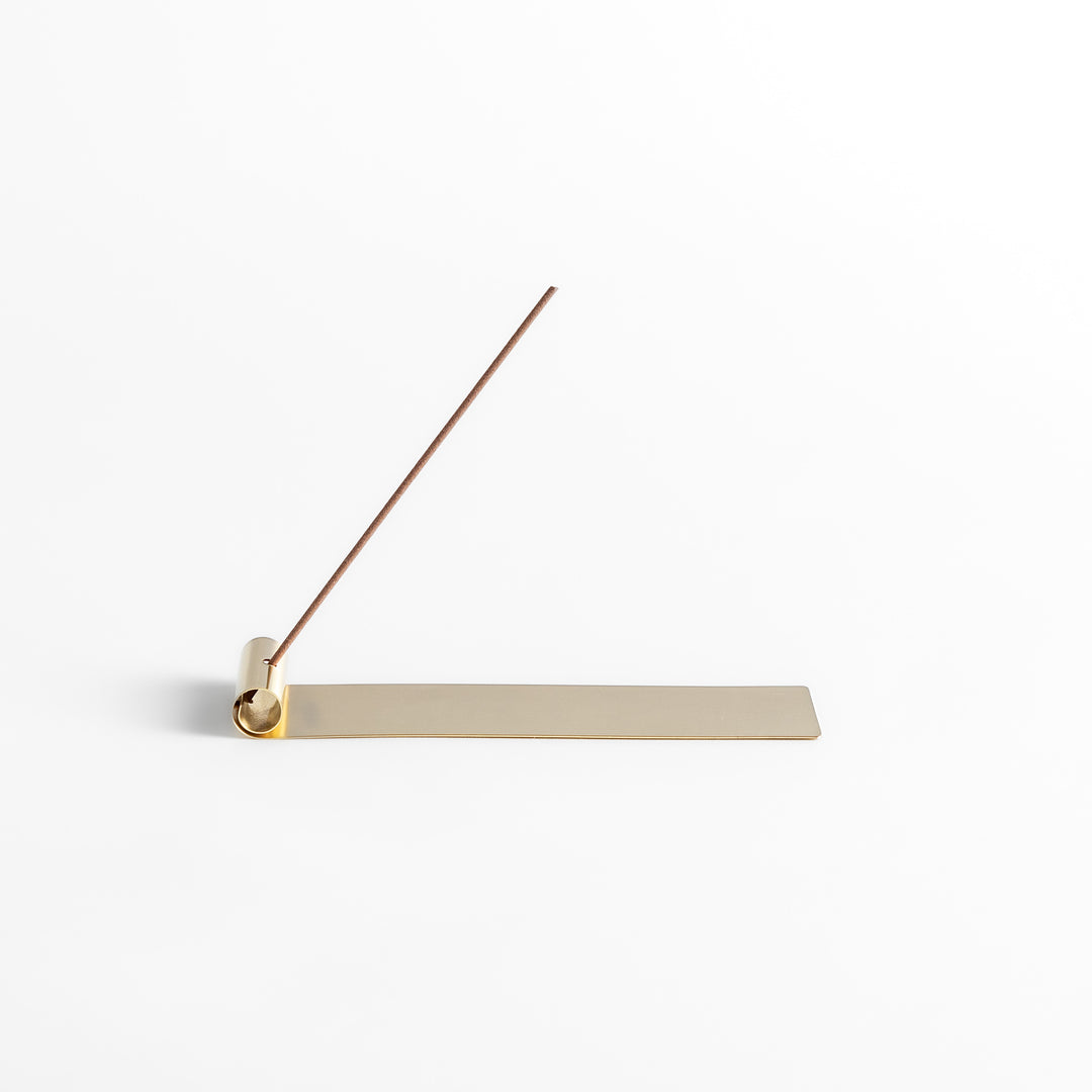 Minimalist brass incense holder with a sleek rolled-edge design, securely holding a single incense stick while the flat base catches falling ash.