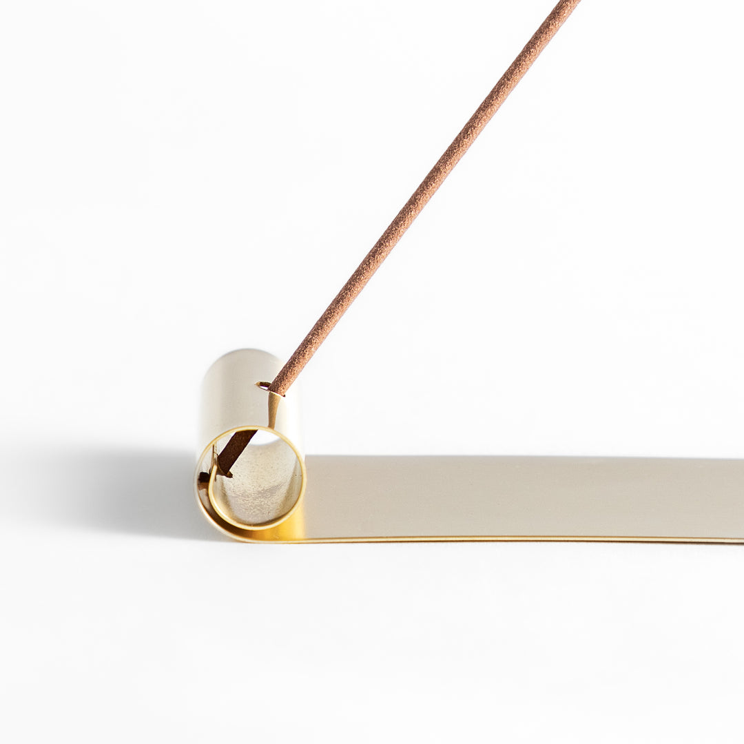 Minimalist brass incense holder with a sleek rolled-edge design, securely holding a single incense stick while the flat base catches falling ash.