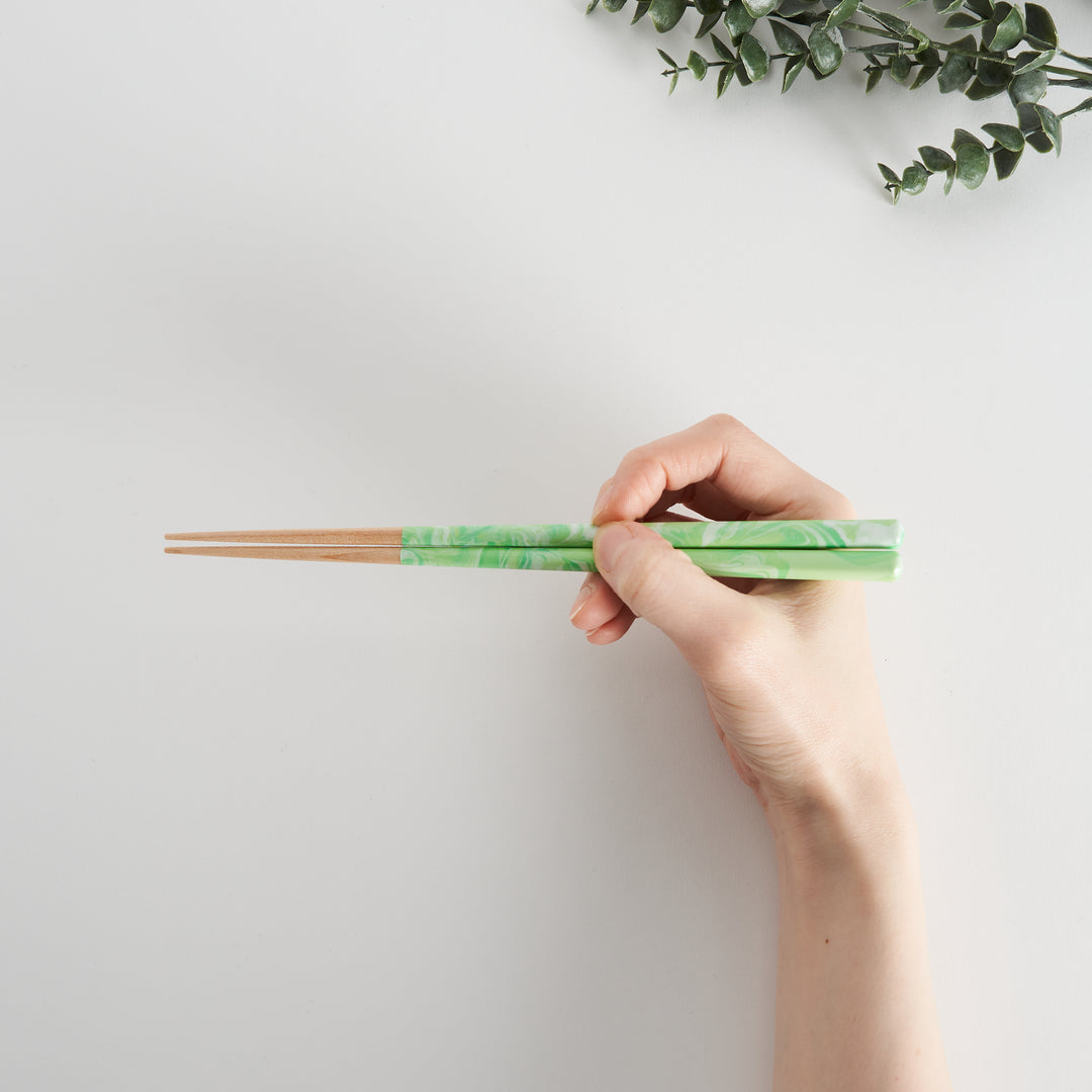 Hand holding mint green marbled chopsticks with wooden tips, showcasing a stylish and functional design with a comfortable grip.