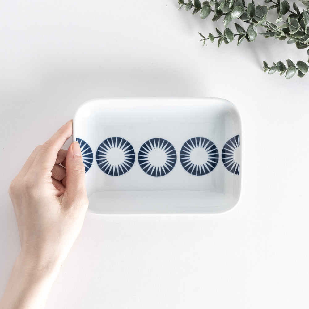 Top view of a rectangular dessert plate held by hand, showcasing the pattern of blue starburst circles on the surface.