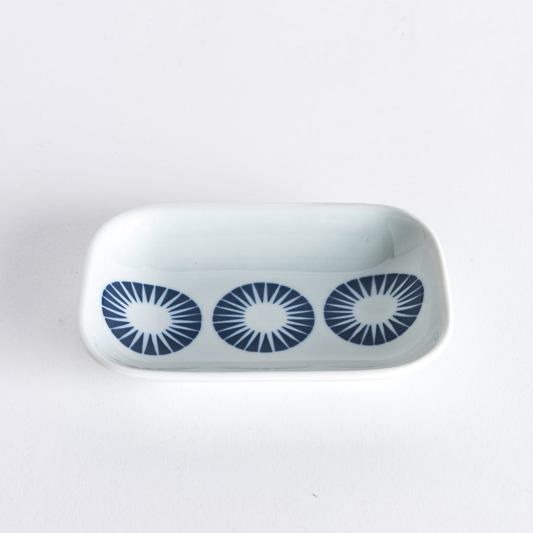 Slightly angled view of the sauce dish showing the navy blue circles with radiating lines, with part of the hand gently holding it.