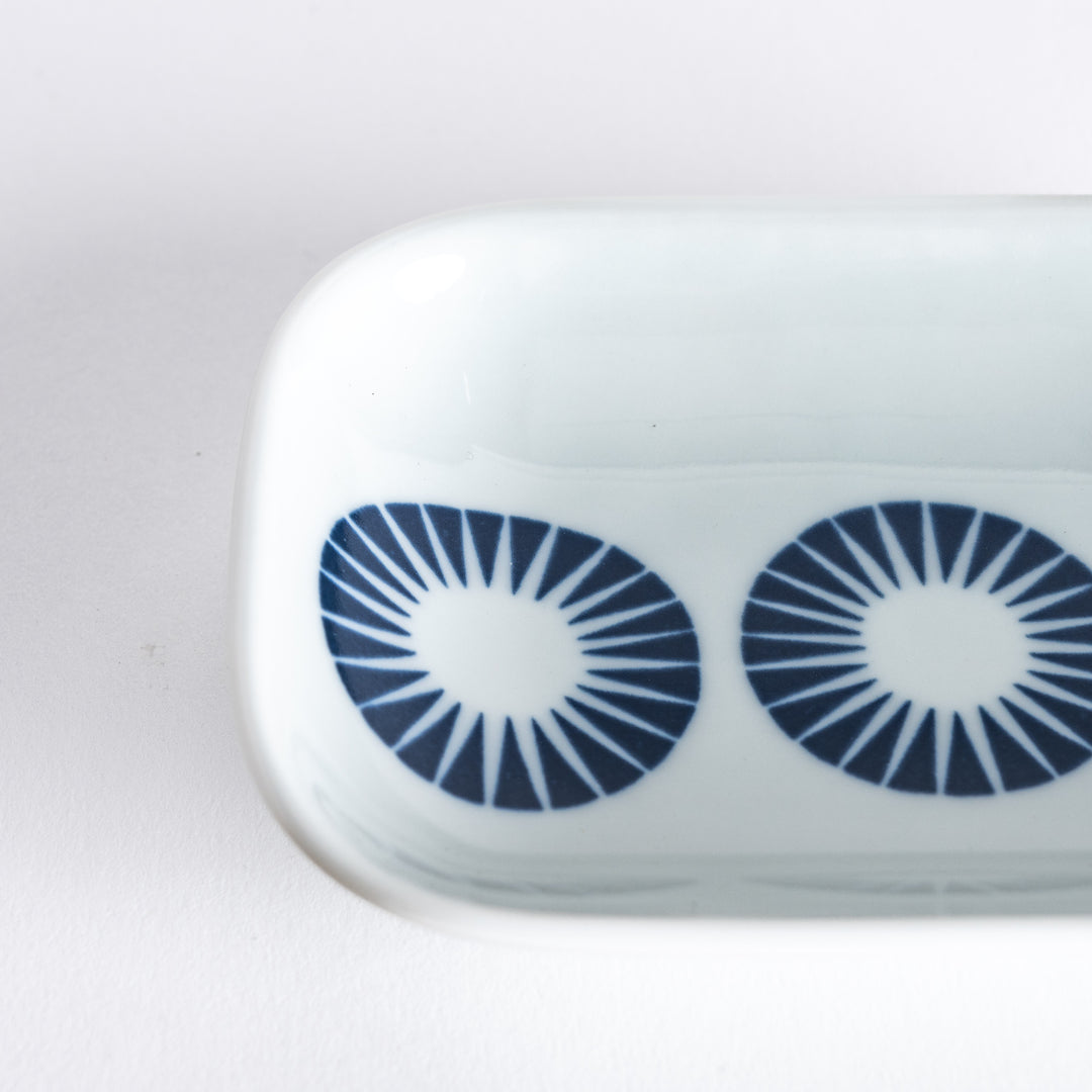 Close-up shot of the sauce dish focusing on the intricate navy blue circle design with radiating lines on the white surface.