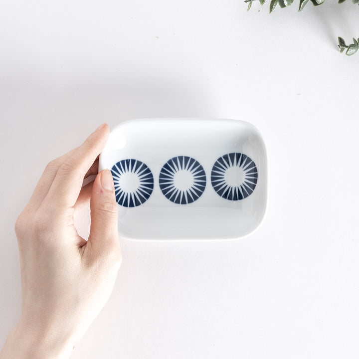 Top view of the sauce dish held in hand, showing three navy blue circles with radiating lines on a white surface.