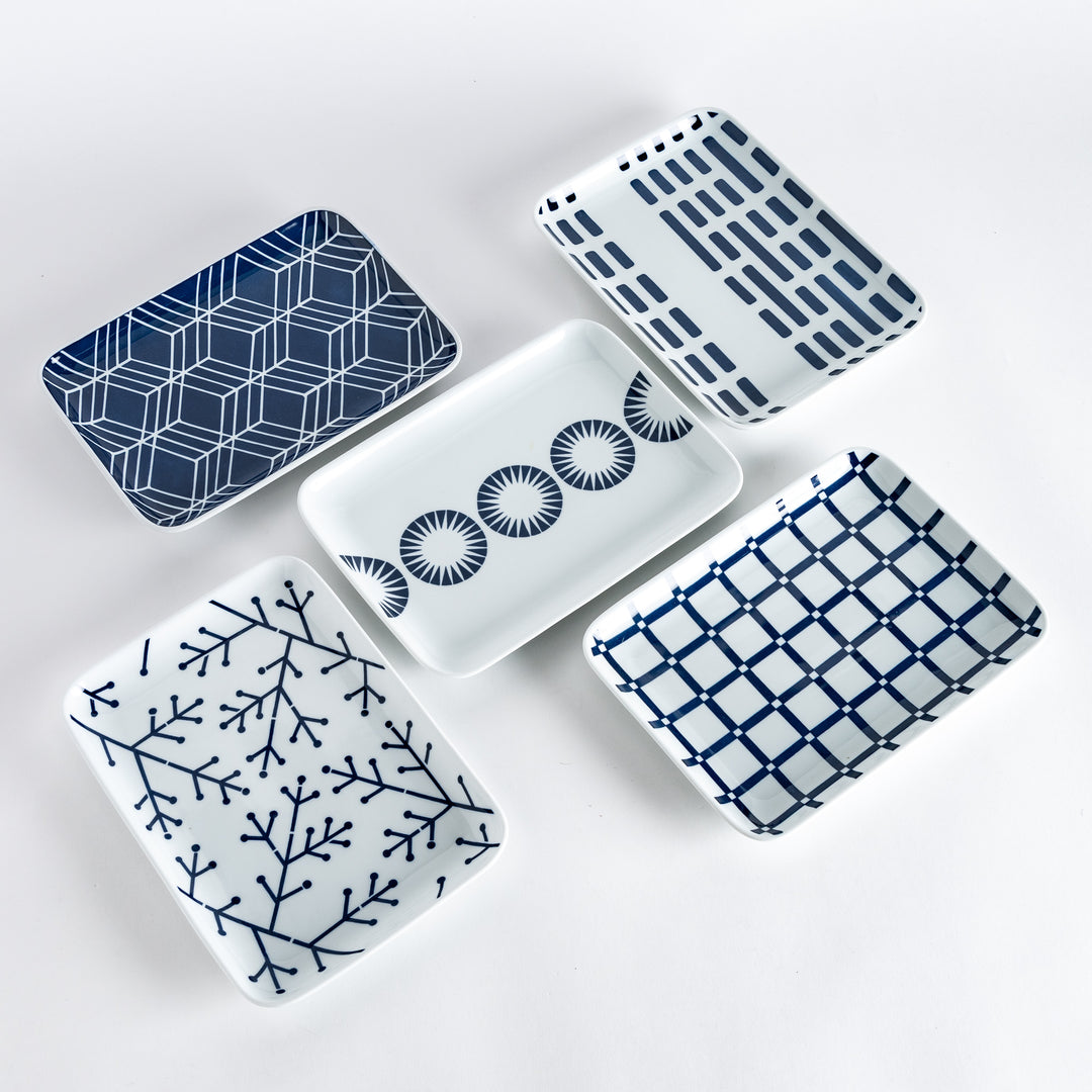 Five different dinner plates with unique indigo patterns, including geometric shapes, lines, and circular designs, on a white background.