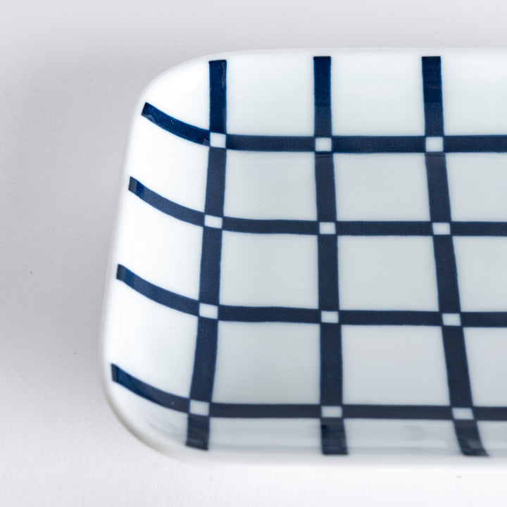 Close-up of the dessert plate's lattice pattern, focusing on the bold navy blue lines creating a grid pattern on the white surface.