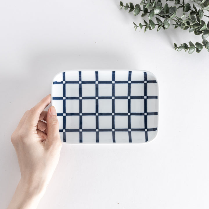 A rectangular dessert plate held by hand, featuring a modern indigo lattice pattern, with navy blue lines creating a grid design.