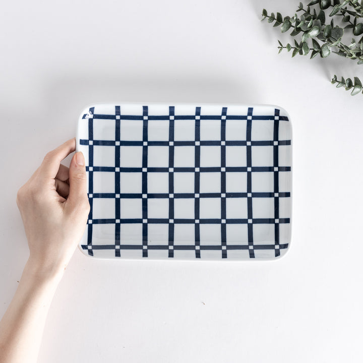 A hand holding the Modern Indigo Lattice Dinner Plate, shown from above. The plate features a navy blue lattice pattern on a white background.