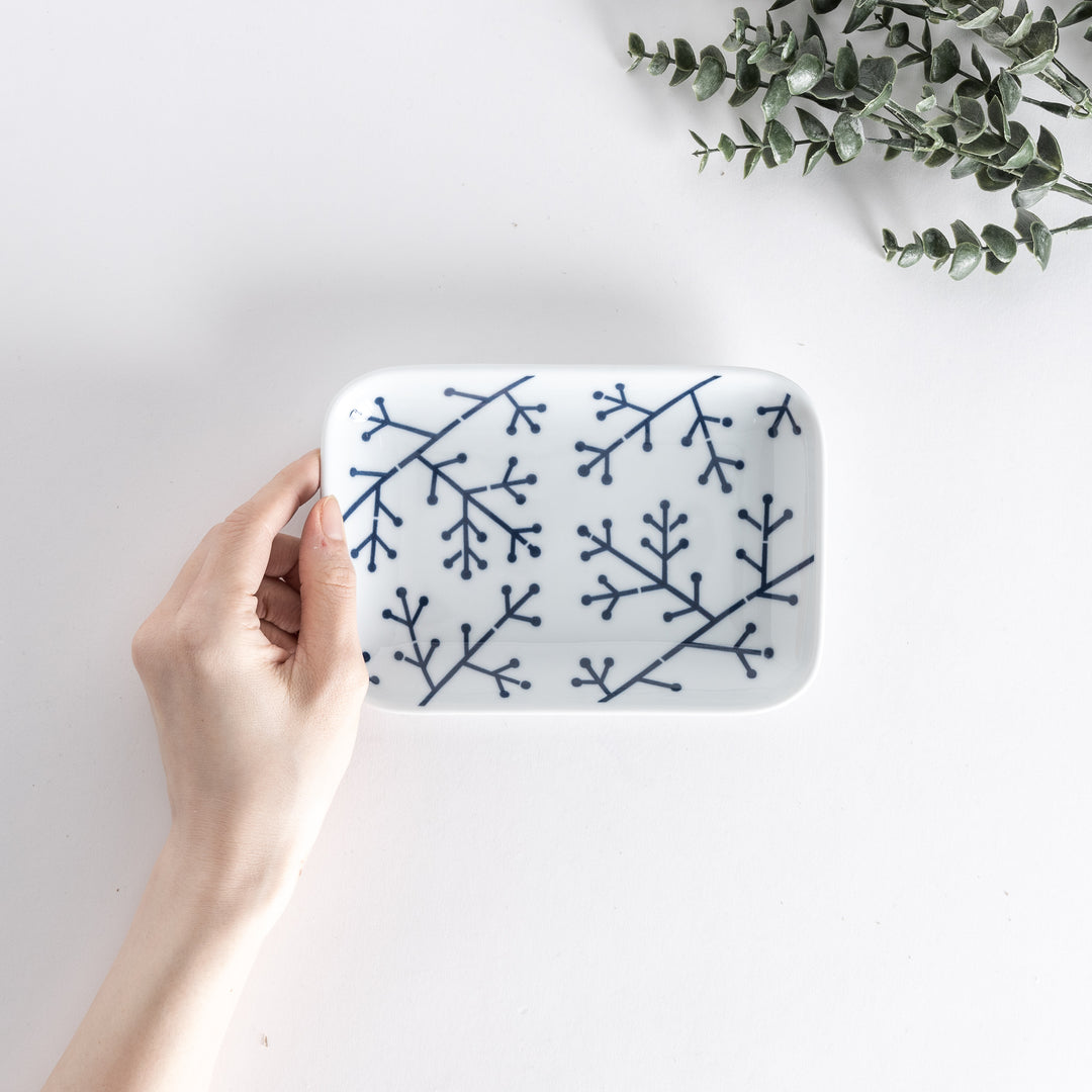 Top view of a dessert plate held in hand, showcasing a modern indigo pine branch pattern on a white surface.