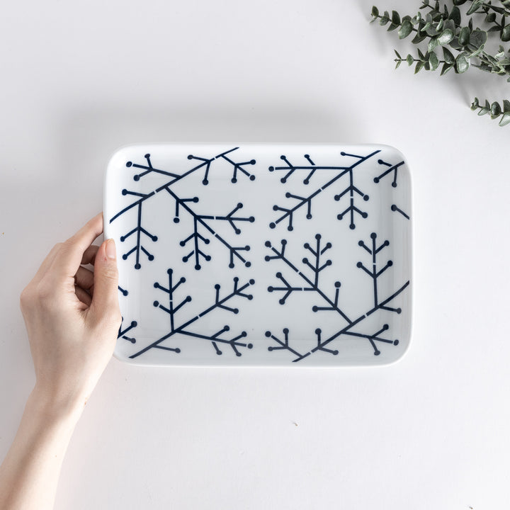 Top-down view of a Modern Indigo Pine Dinner Plate held in hand, showcasing the navy blue pine branch design on a white background.