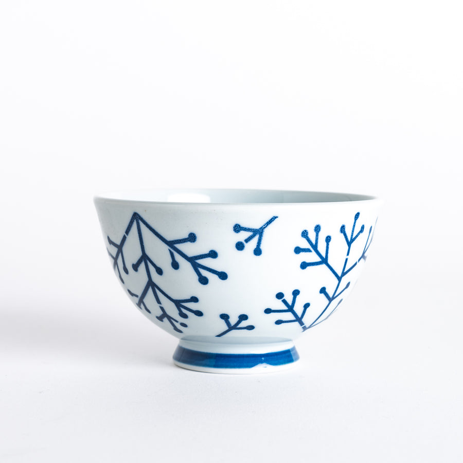 A side view of the Modern Indigo Pine Rice Bowl, showcasing the navy blue pine branch design on a white background and the blue base.