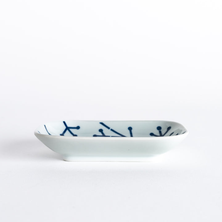 Side view of the sauce dish with a subtle navy blue pine branch pattern across its white surface.