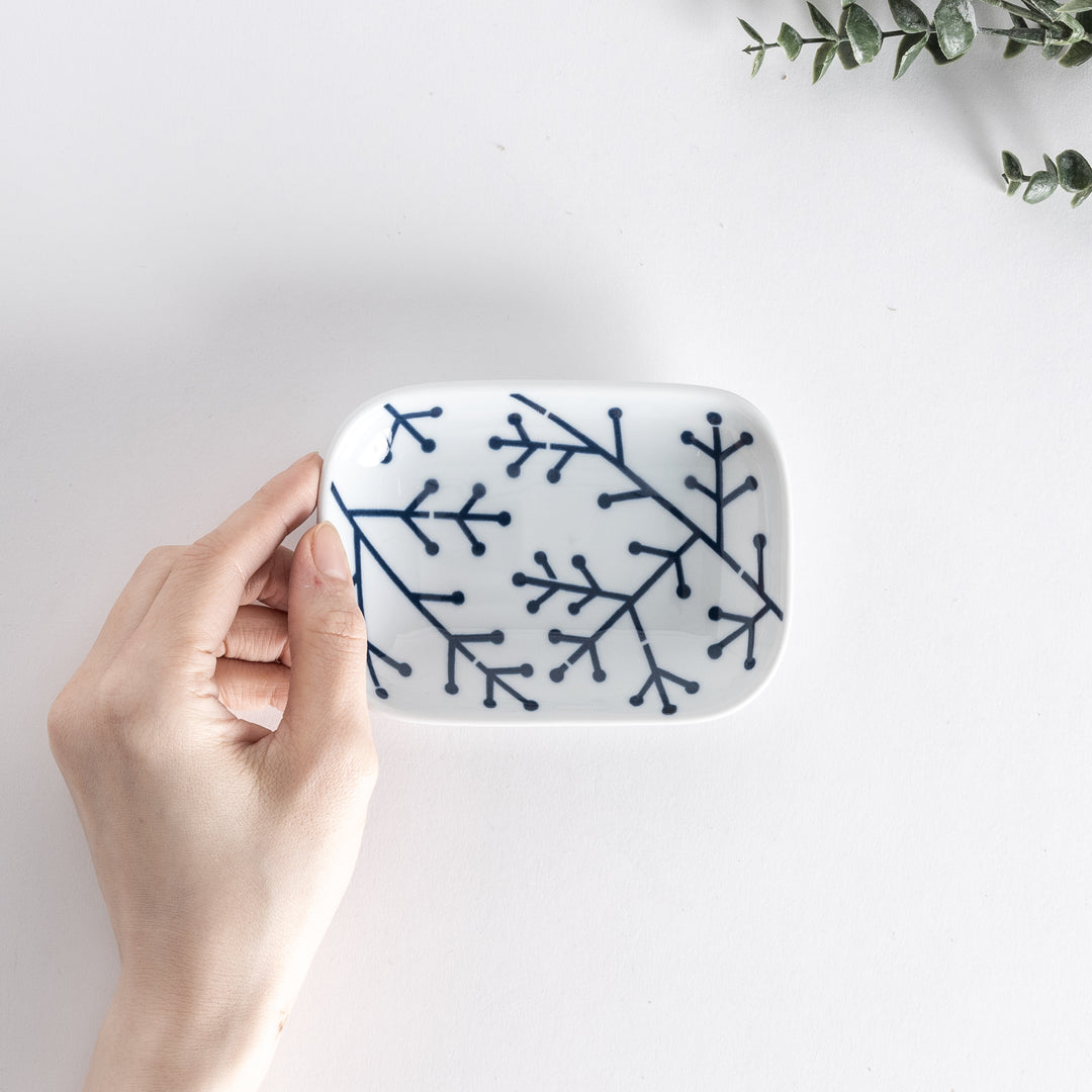 Top view of the sauce dish featuring a navy blue pine branch pattern against a white background, held in hand.