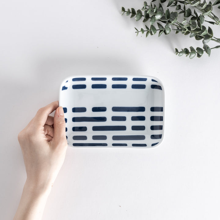 Top view of a hand holding a rectangular dessert plate with modern blue river-like line patterns.