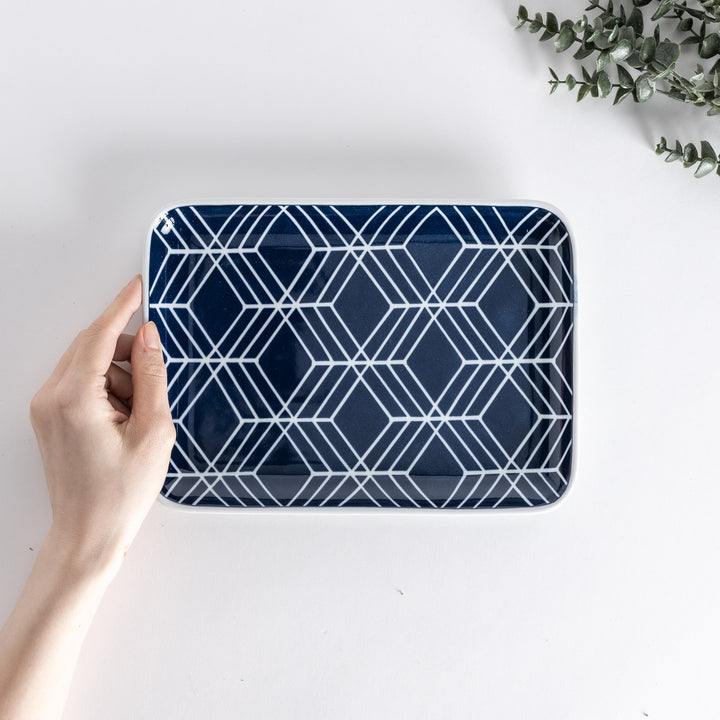 Handheld top-down view of the Modern Indigo Tile Dinner Plate showing geometric white diamond patterns on a deep navy blue background.