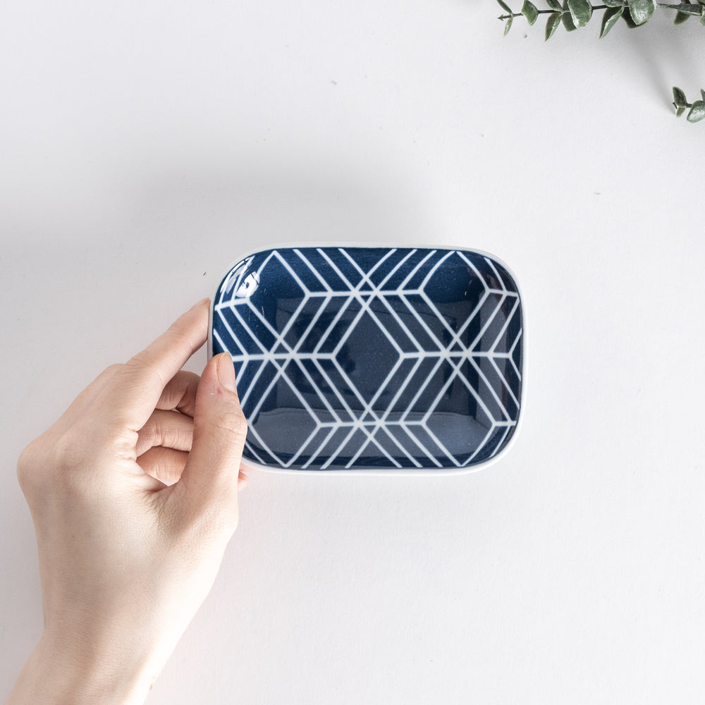 Top view of sauce dish held by hand, featuring a modern geometric pattern in navy blue on a white background.