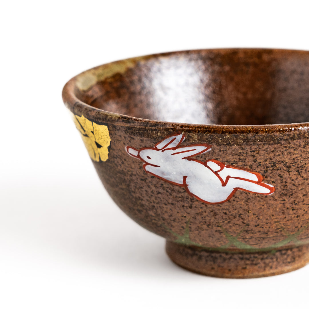 Brown ceramic sake cup with a playful rabbit design and a unique crackled glaze, perfect for enjoying a traditional cup of sake.