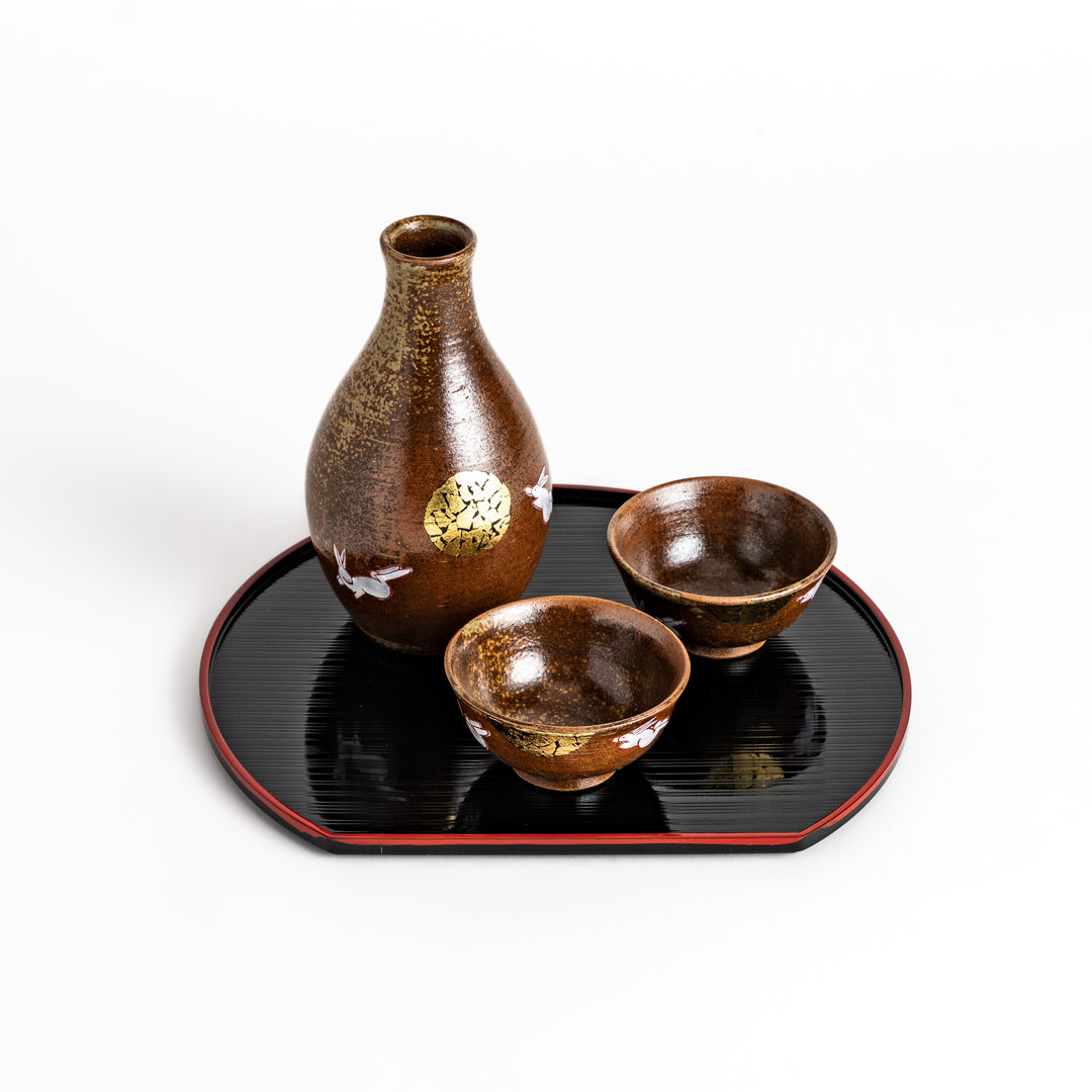 Brown ceramic sake set with a rabbit and moon design, including a sake carafe and two cups presented on a serving tray, perfect for enjoying sake with a friend.